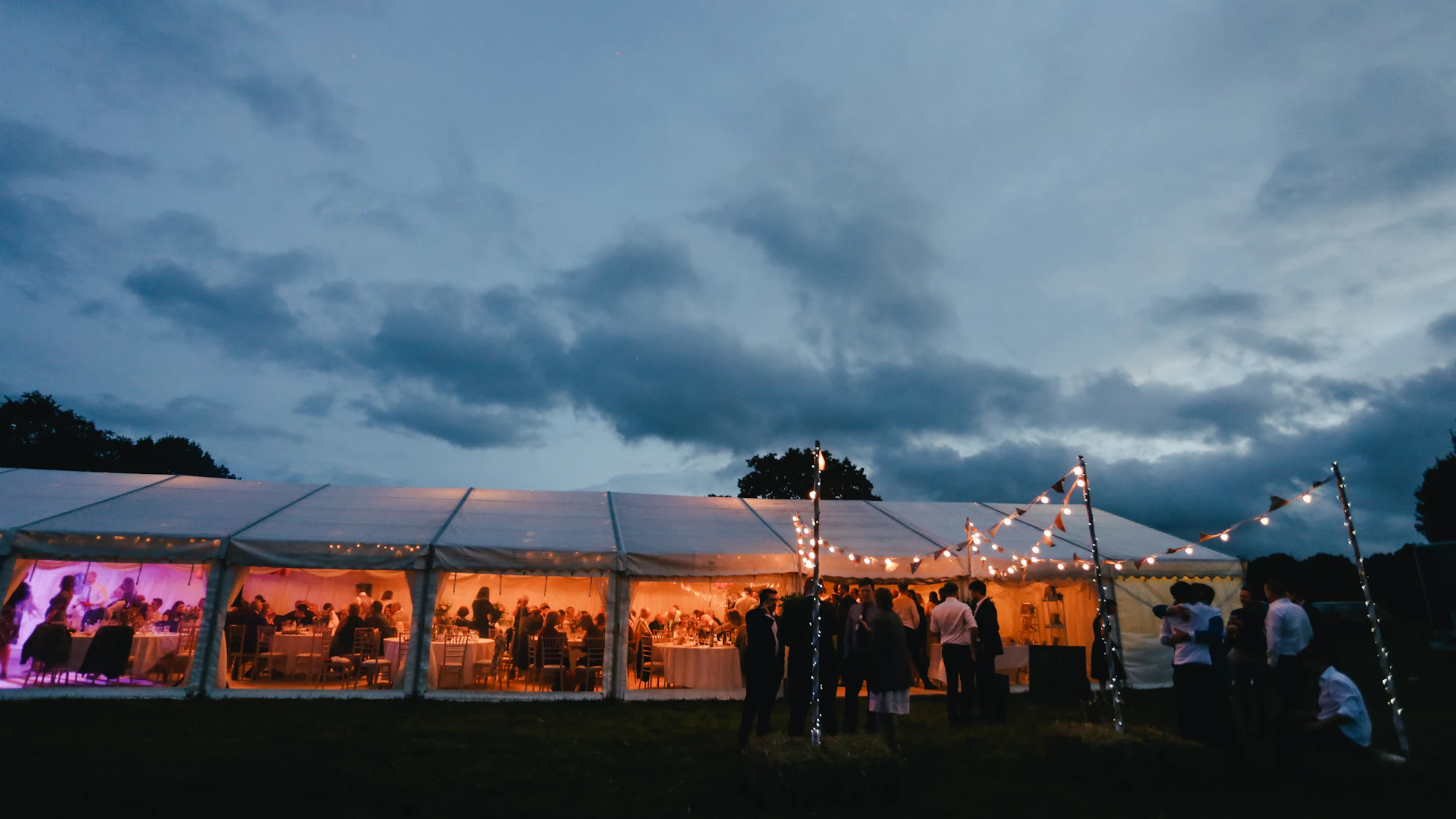 Marquee glowing with fairy lights as guests celebrate at dusk