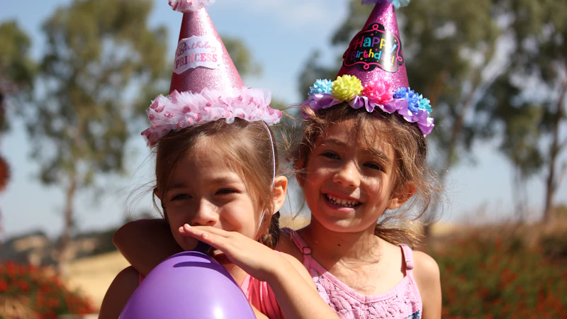 Two girls in party hats laughing with balloons outdoors