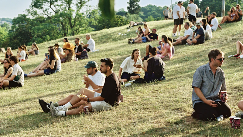 Festival-goers relaxing on a golden grassy slope at a summer village event