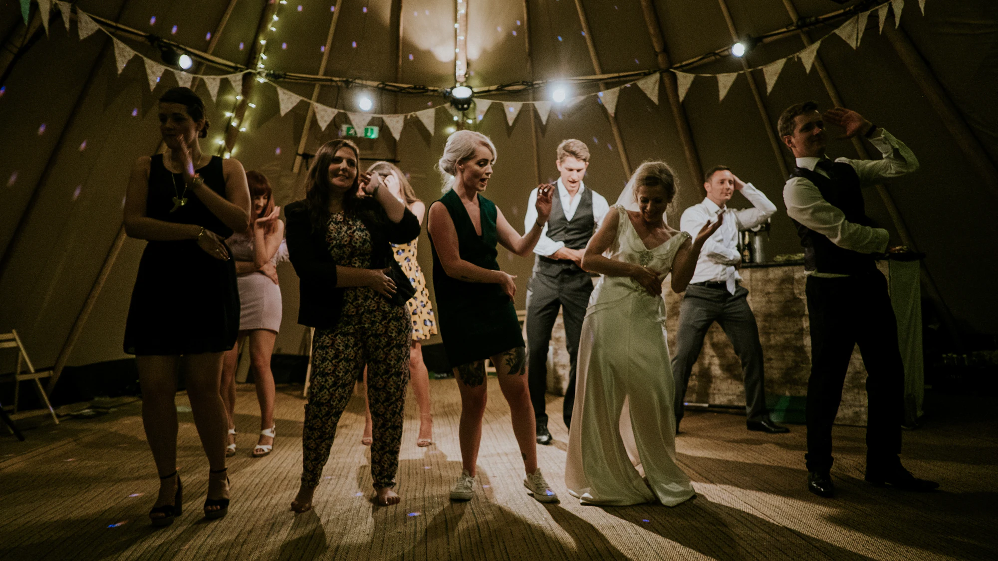 Bride and guests dancing under bunting inside a wedding marquee